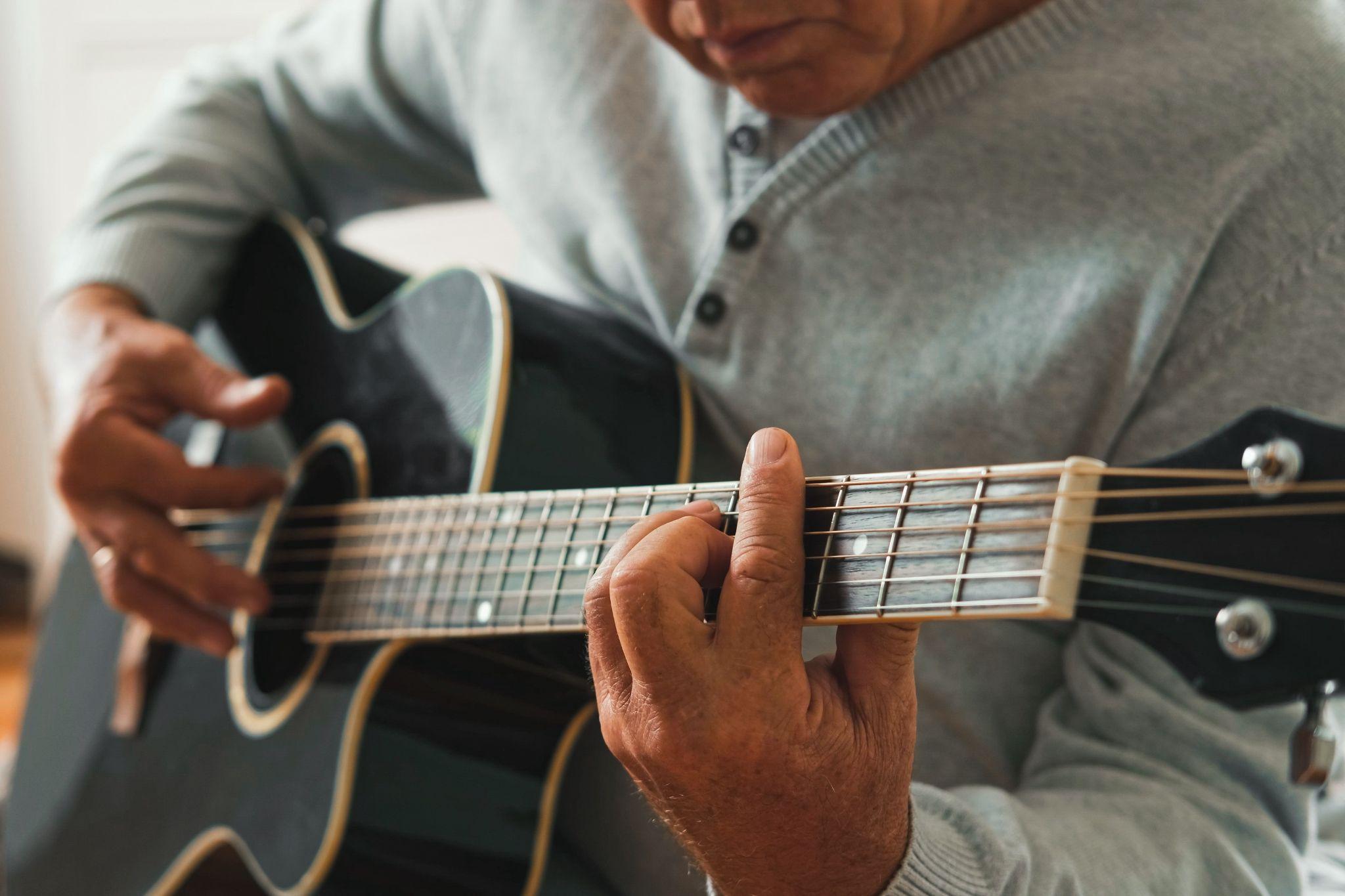 An older adult sitting down and playing guitar to support brain health.